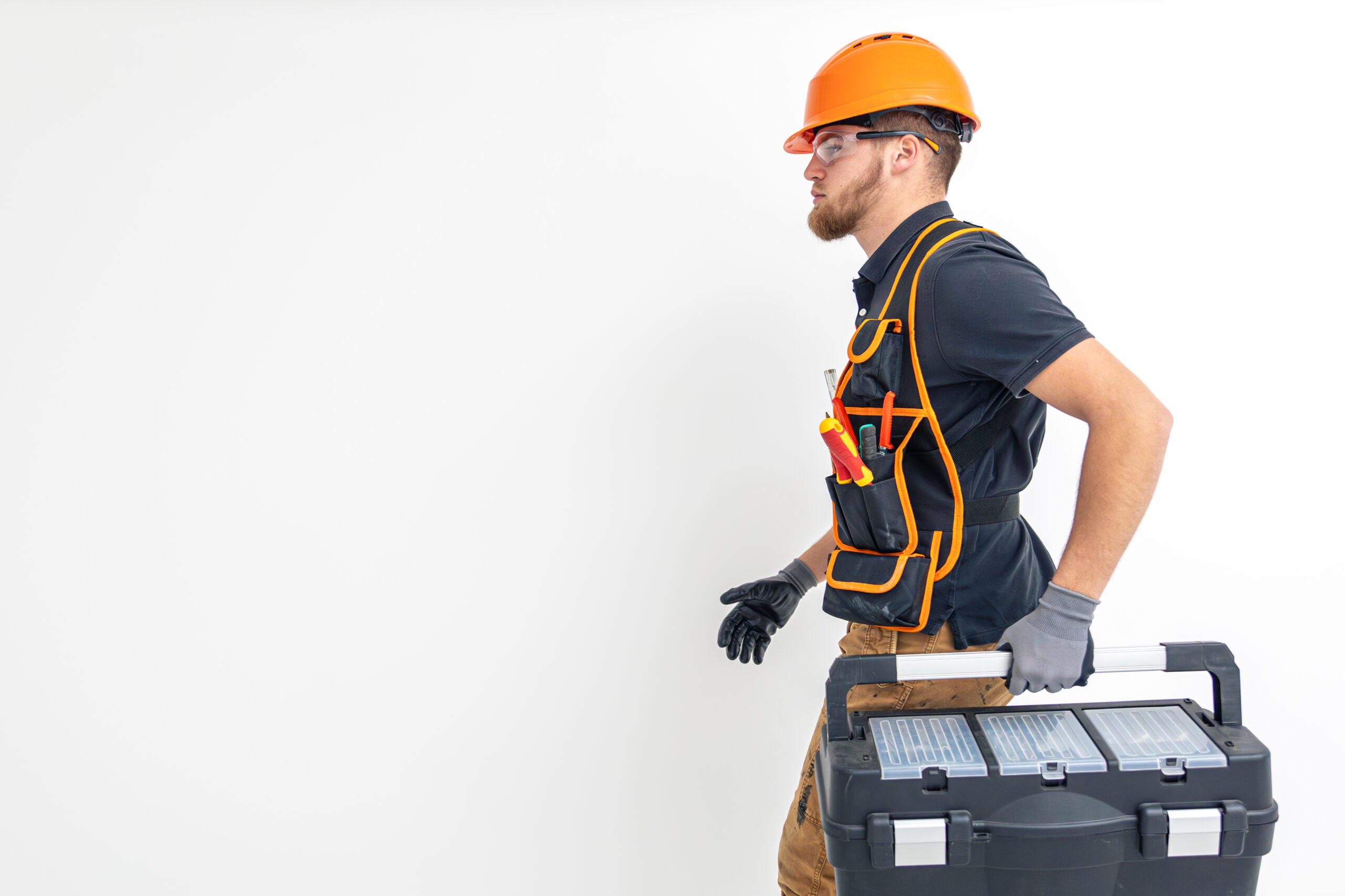 Male builder. Electrical engineer in overalls and helmet holds toolbox in hands. Light background. Construction concept. Space for text. High quality photo.